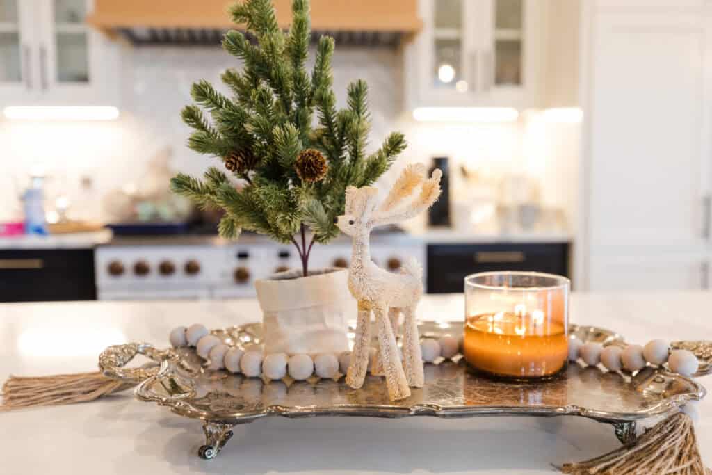 Festive holiday centerpiece with a small pine tree, reindeer figurine, and candle on a tray.