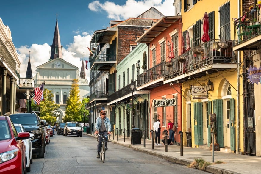 Vibrant French Quarter street with colorful buildings, balconies, and pedestrians in New Orleans.