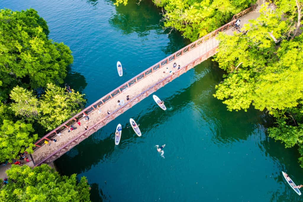 Barton Springs Austin Texas USA Aerial drone views above the Barton Creek Bridge as crowds of people walk across the bridge and Kayakers go under and swimmers swim in the cold refreshing waters fed by Cold Springs