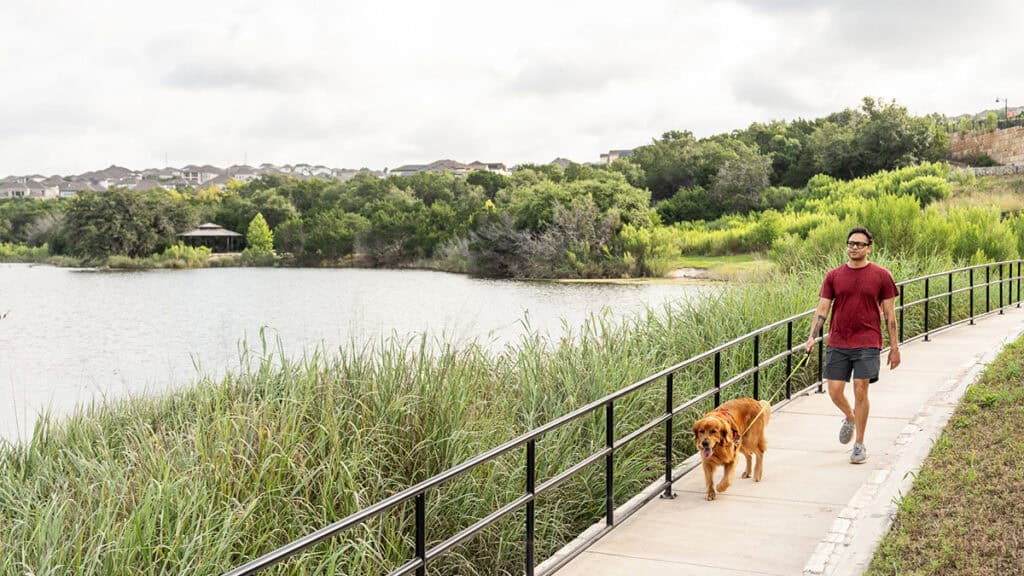 Man walking dog along Travisso community lake trail on a cloudy day.