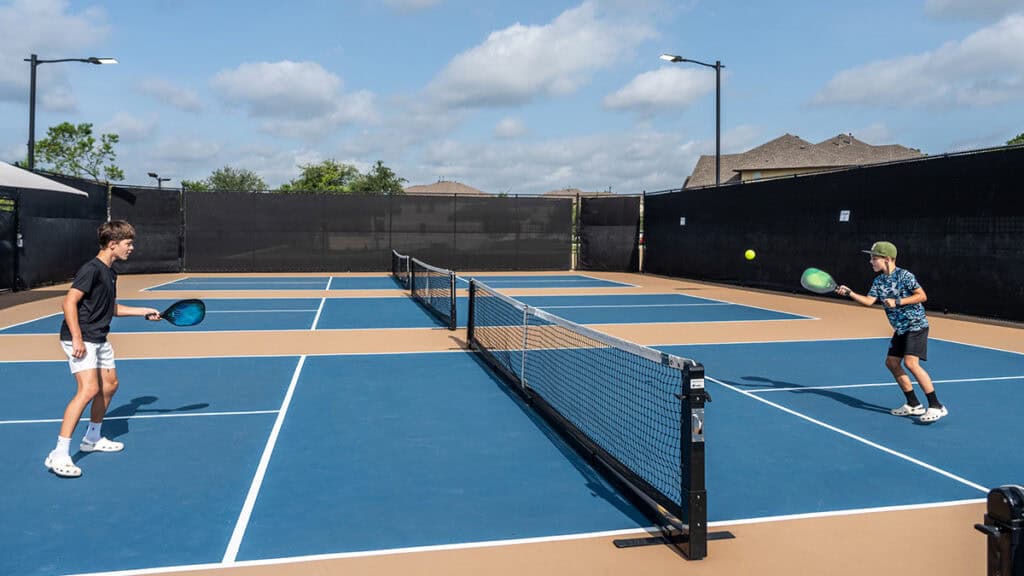 Two children playing tennis on Travisso community courts in bright sunlight.