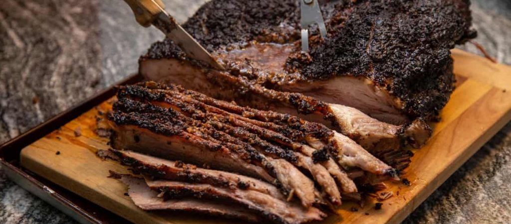 A juicy beef brisket, fresh off the smoker, being sliced on a board on the counter, for a weekend dinner at the cottage. part of series